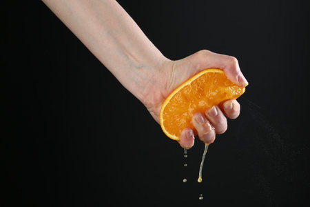 Woman squeezing orange on black background, closeupの写真素材