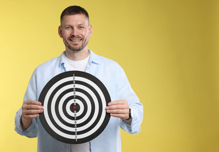 Targeting. Man with dart board on yellow background, space for text