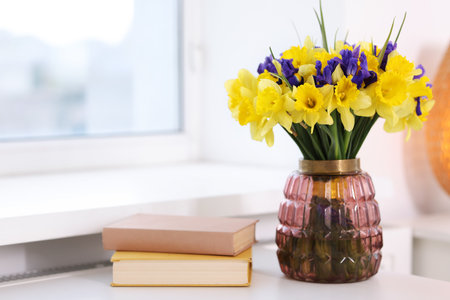 Bouquet of beautiful flowers in vase and books on desk near window indoorsの写真素材