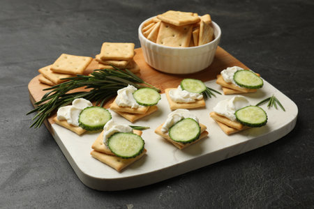 Tasty crackers with cream cheese, rosemary and cucumber on dark textured table, closeupの写真素材