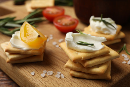 Tasty crackers with cream cheese, rosemary, salt and tomatoes on wooden table, closeupの写真素材