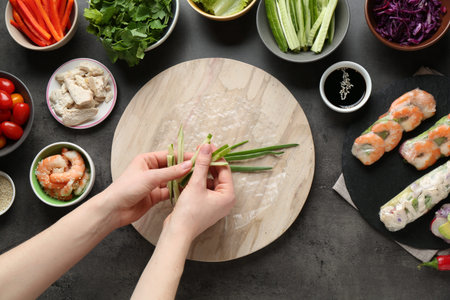 Woman making tasty spring roll at dark gray table, top view