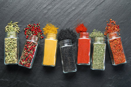 Different aromatic spices in jars on black table, flat layの写真素材