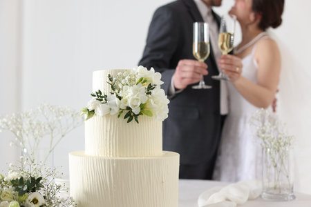 Married couple together indoors, focus on wedding cake and bouquet on tableの写真素材