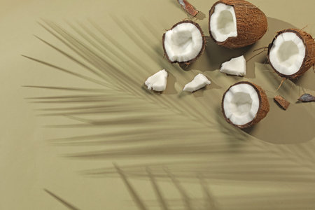 Fresh coconuts and shadow cast by tropical palm on light green background, flat lay. Space for text
