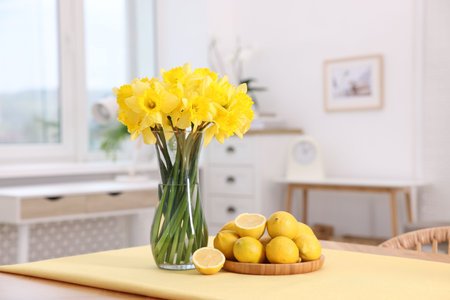 Beautiful daffodils in vase and lemons on wooden table at homeの写真素材