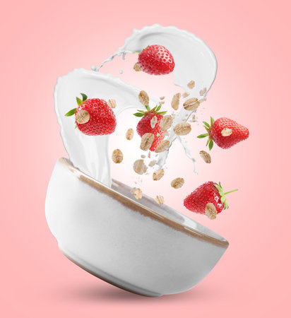 Oat flakes with fresh strawberries and milk splashing out from bowl in air on pink backgroundの写真素材