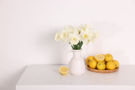 Beautiful daffodils in vase and lemons on white wooden table. Space for textの写真素材