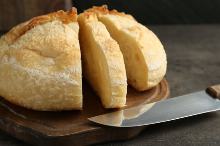 Slices of fresh bread and knife on dark textured table, closeup