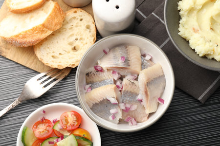 Delicious herring pieces with onions served on black wooden table, flat layの写真素材