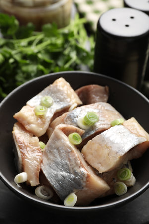 Pieces of delicious herring with green onions on black table, closeupの写真素材