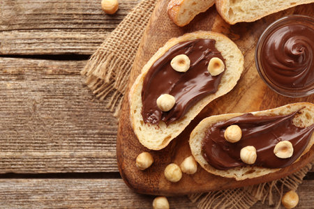 Slices of bread with chocolate spread and hazelnuts on wooden table, flat lay. Space for textの写真素材