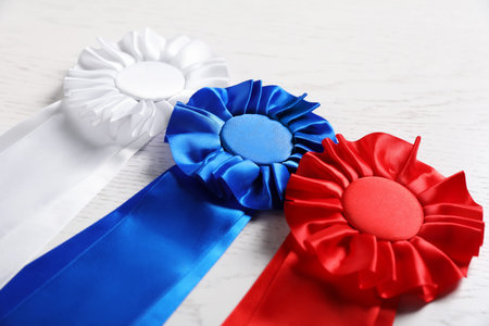 Different award ribbons on white wooden table, closeup. Space for text