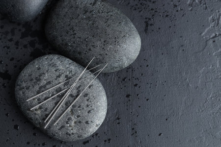 Acupuncture needles and wet spa stones on dark textured background, flat lay. Space for textの写真素材