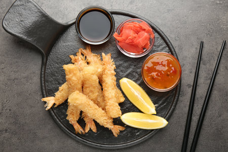 Tasty tempura shrimps served with lemon, ginger and sauces on grey textured table, flat lay