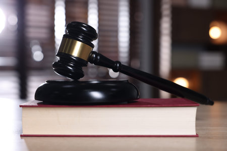 Judge's gavel, sound block and book on wooden table against blurred background, closeup