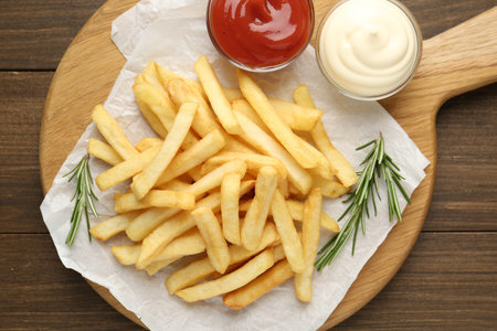 Tasty french fries with sauces and rosemary on wooden table, top view