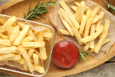 Tasty French fries served with ketchup and rosemary on wooden table, top view