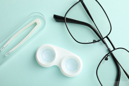 Contact lenses in case, tweezers and glasses on light turquoise background, flat layの写真素材