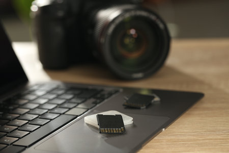 SD memory cards, holder, laptop and photo camera on wooden table, closeupの写真素材