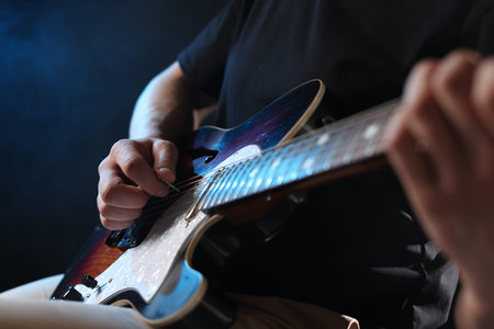 Man playing guitar with mediator on dark background, focus on hand