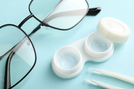 Contact lenses in case, tweeters and glasses on light turquoise background, above viewの写真素材