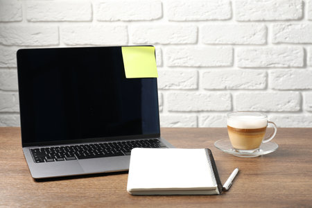 Laptop with sticky note, notebook, coffee and pen on wooden table. Space for textの写真素材