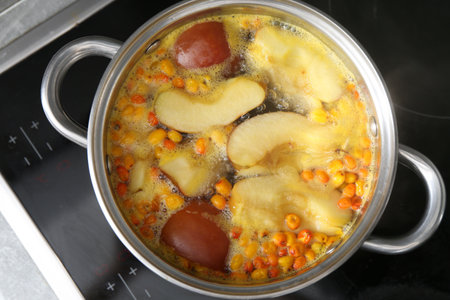Making compot of apples and sea buckthorn berries. Simmering fruits in pot on stove, top viewの写真素材