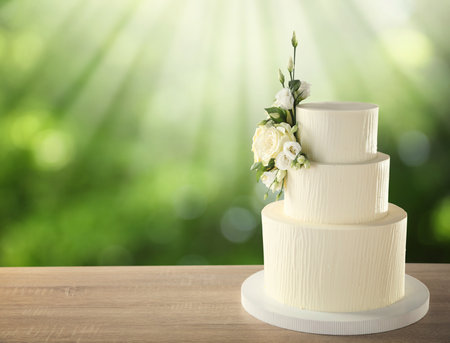 Beautiful wedding cake with floral decor on wooden table outdoors. Space for textの写真素材