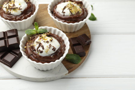 Tasty pudding with whipped cream in bowls and pieces of chocolate on white wooden table, closeup. Space for textの写真素材