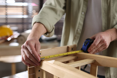 Man measuring wooden stool with tape indoors, closeupの写真素材