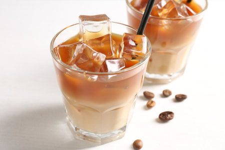 Tasty iced coffee and beans on white table, closeup