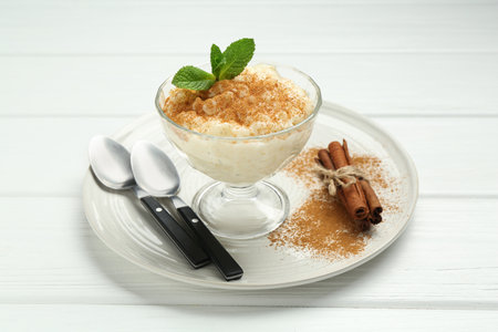 Delicious rice pudding with cinnamon, mint and spoons on white wooden tableの写真素材