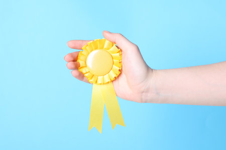 Woman holding yellow award ribbon on light blue background, closeupの写真素材
