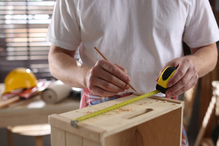 Man measuring wooden shelf with tape and pencil indoors, closeupの写真素材