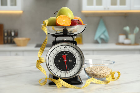 Kitchen scales with fruits, measuring tape and oatmeal in bowl on light marble table indoorsの写真素材