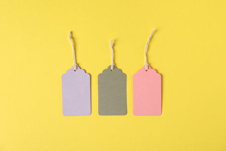 Blank tags with strings on yellow background, flat lay