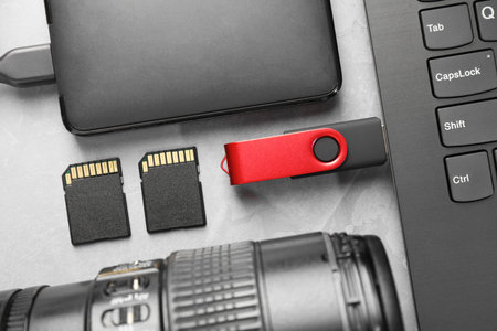 Flash drive connected to laptop, SD memory cards, external hard disk and camera lens on gray...