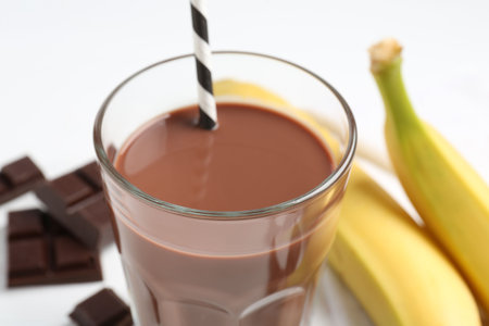 Tasty chocolate milk in glass, pieces and bananas on white table, closeupの写真素材