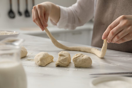 Making pretzels. Woman shaping dough at table in kitchen, closeup