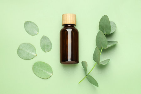 Bottle of essential oil and eucalyptus leaves on green background, flat layの写真素材