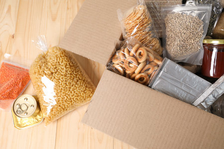 Different food products in box on wooden table, flat lay
