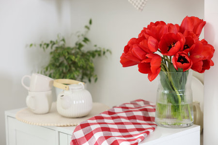 Beautiful red tulips in vase, cups and teapot on cabinet indoorsの写真素材