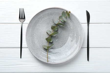 Stylish plate, cutlery and eucalyptus branch on white wooden table, flat layの写真素材