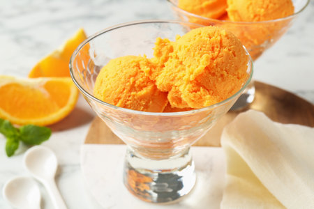 Balls of tasty orange sorbet in dessert bowls, fresh fruit and mint on table, closeupの写真素材