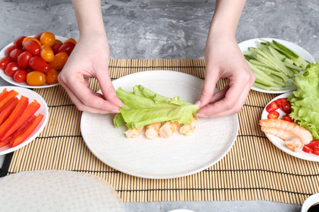 Woman making tasty spring roll at light grey table, closeupの写真素材