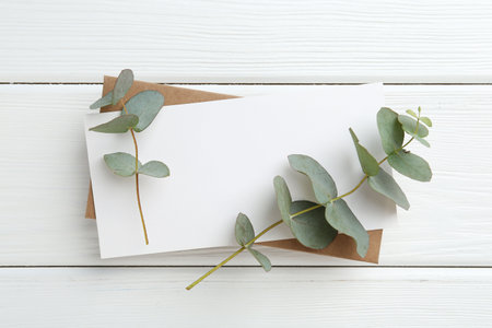Blank card and eucalyptus branches on white wooden table, top viewの写真素材
