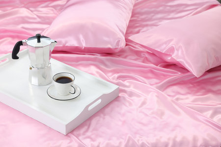 Moka pot and cup of coffee on bed with silk linensの写真素材