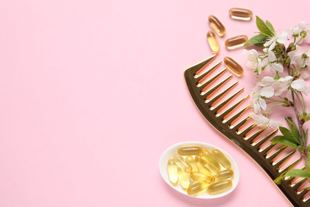 Collagen capsules, blossoms and comb on pink background, flat lay. Space for textの写真素材