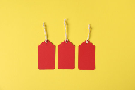 Blank tags with strings on yellow background, flat lay